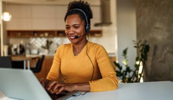 Smiling woman, working online, using earphones and laptop.