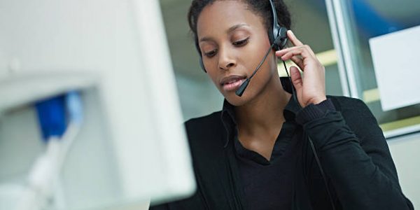 female african american customer service representative with headset typing on computer. Horizontal shape, front view, waist up