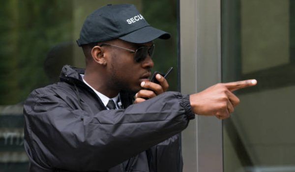 Young Male Security Guard Gesturing While Talking On Walkie-Talkie